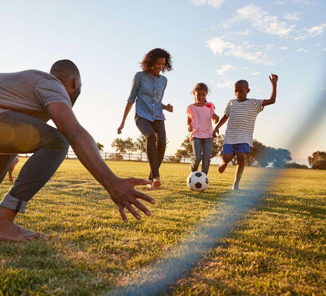 A family smiles and plays soccer in a bright, sunny field
